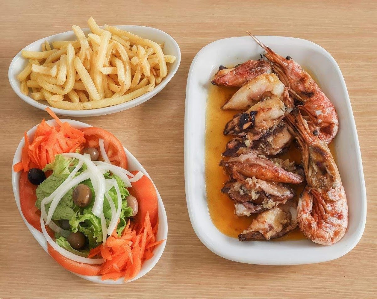 Travessa de lulas e gambas grelhadas na brasa, com batata frita e salada mista ao lado.